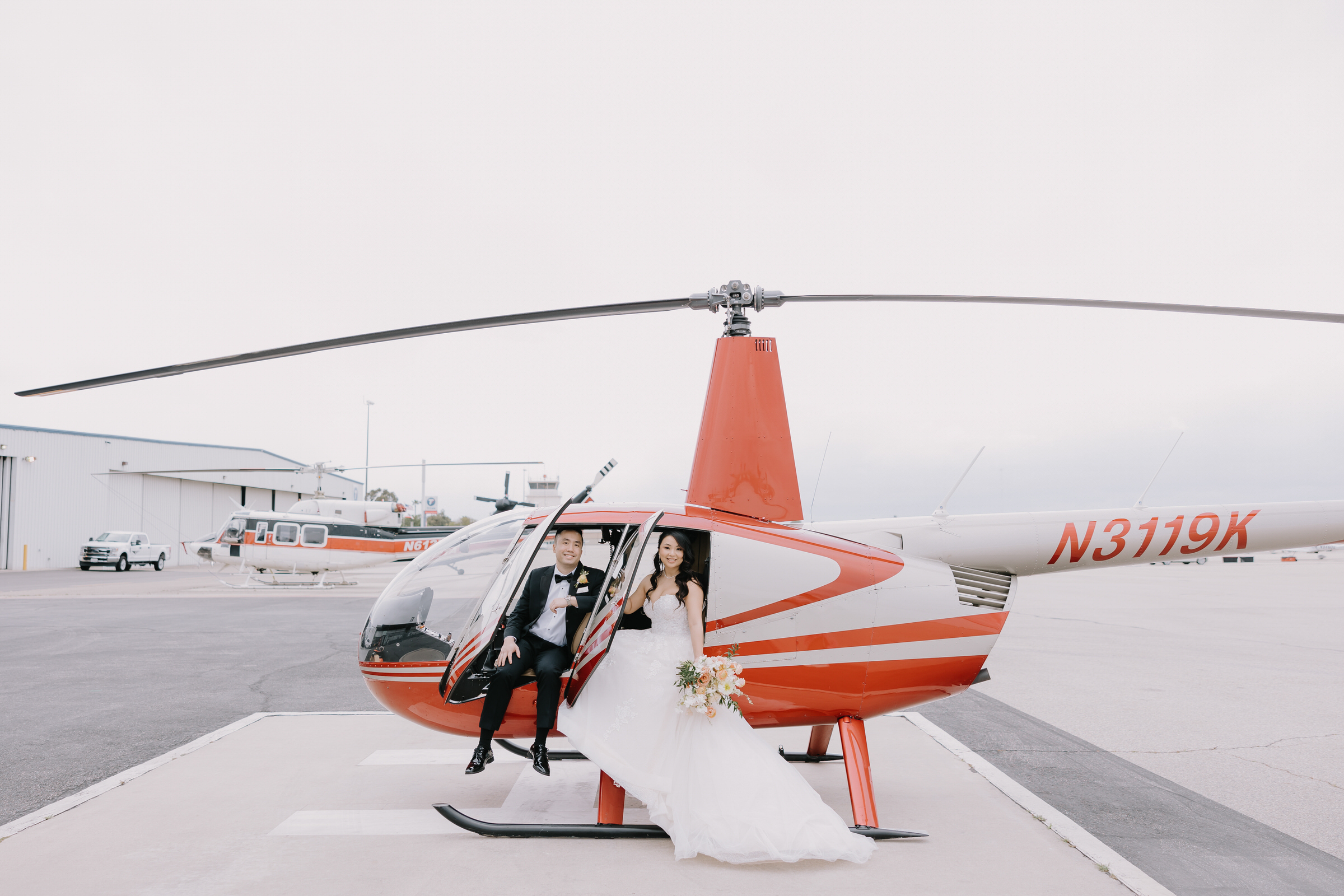Anna and Chris posing in front of a helicopter at their Hangar 21 Fullerton wedding.