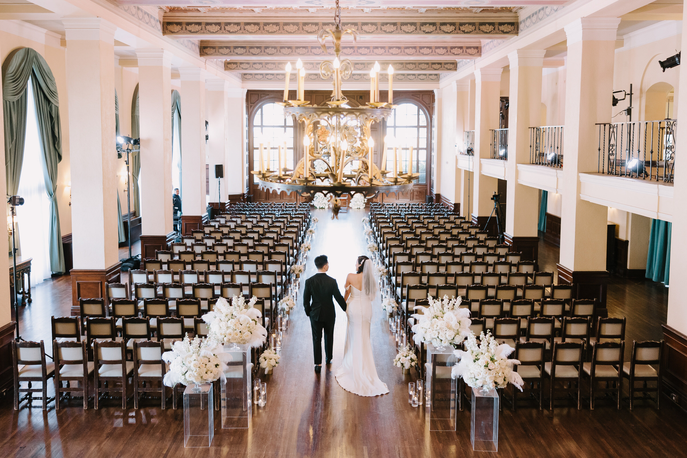 Kristeen and Nick smiling at their Ebell of Los Angeles wedding reception featuring extravagant floral arrangements and ornate architecture.