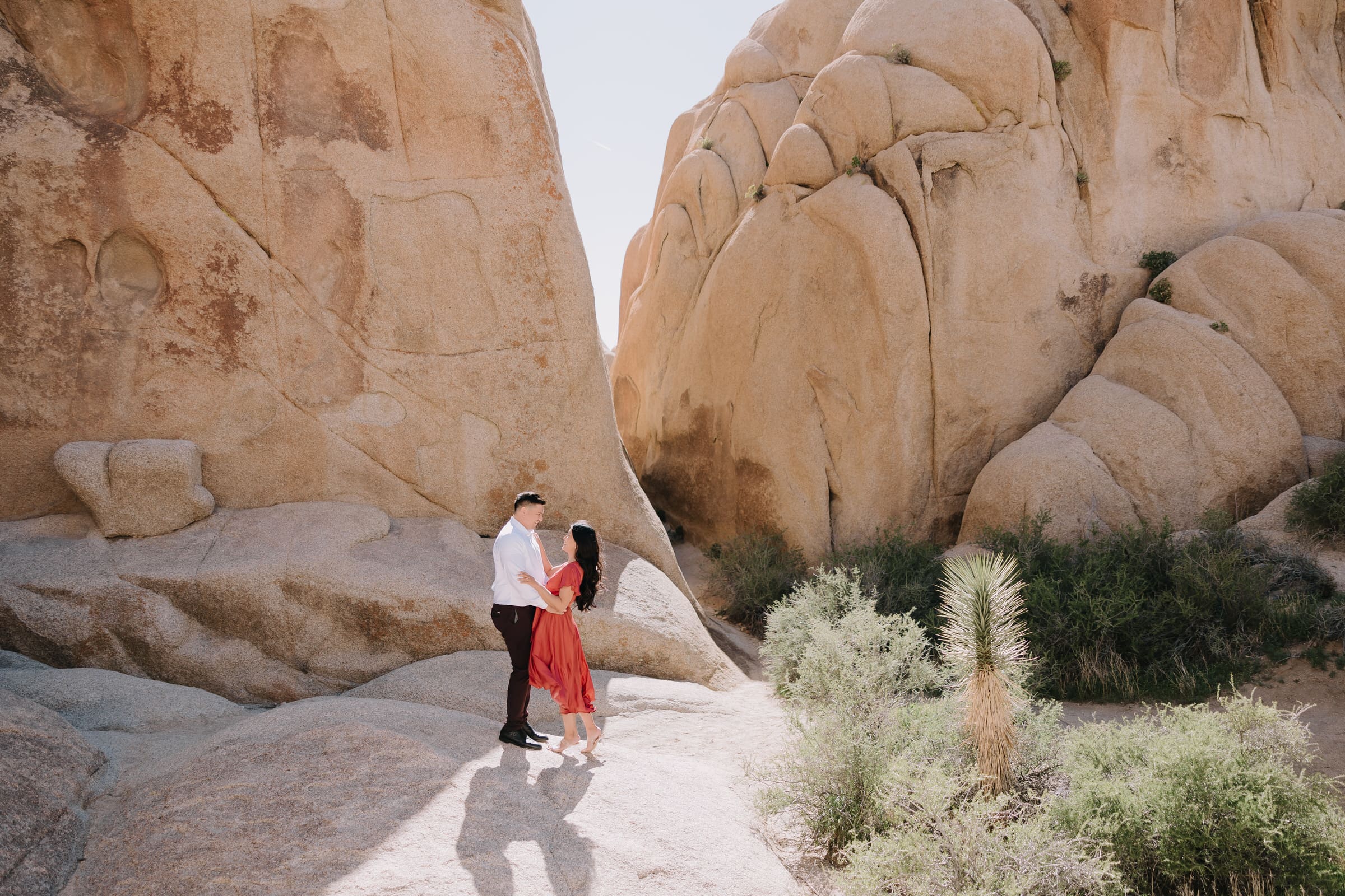 An adventurous couple, Alyssa and Marc, hiking and embracing during their Joshua Tree engagement session at sunset.