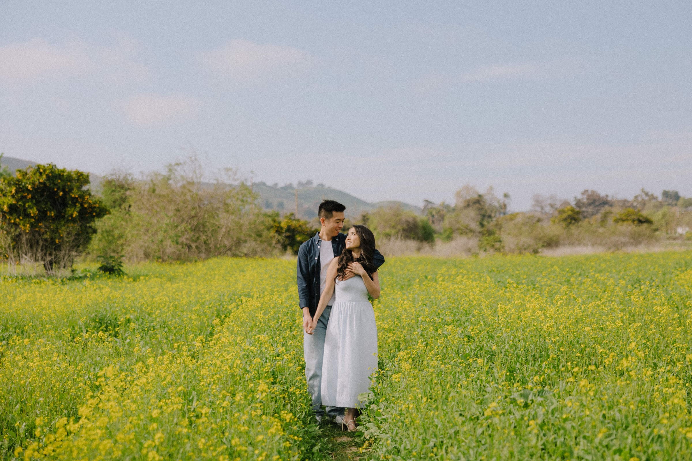 Mai and Nate laughing in a field of yellow mustard plants during the San Juan Capistrano super bloom.