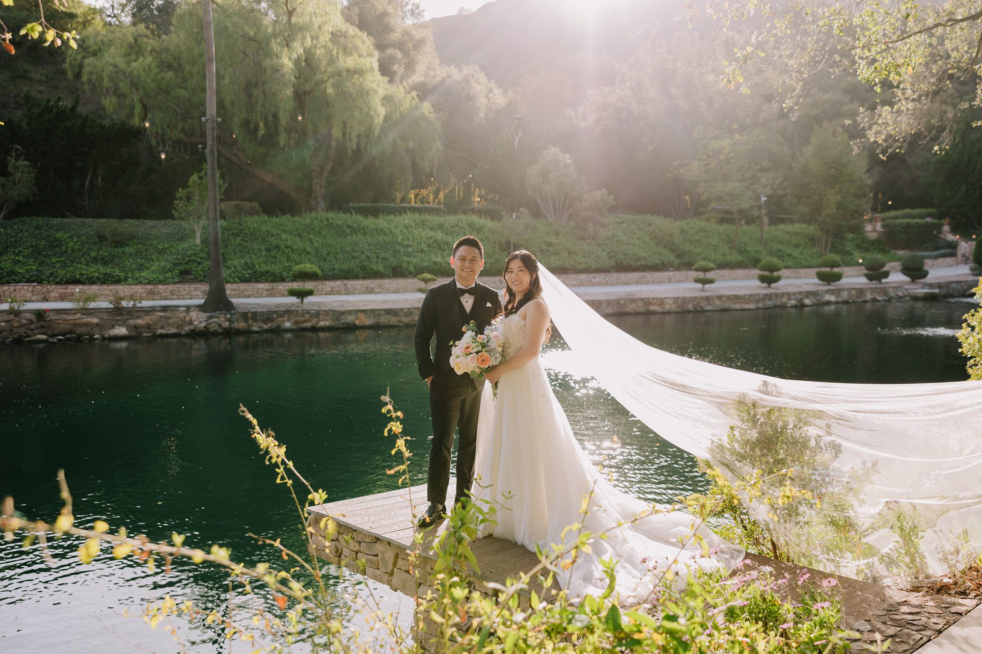 Bride and groom standing under massive oak trees in the lush green meadow at Los Willows Wedding Estate during a sunny outdoor ceremony.