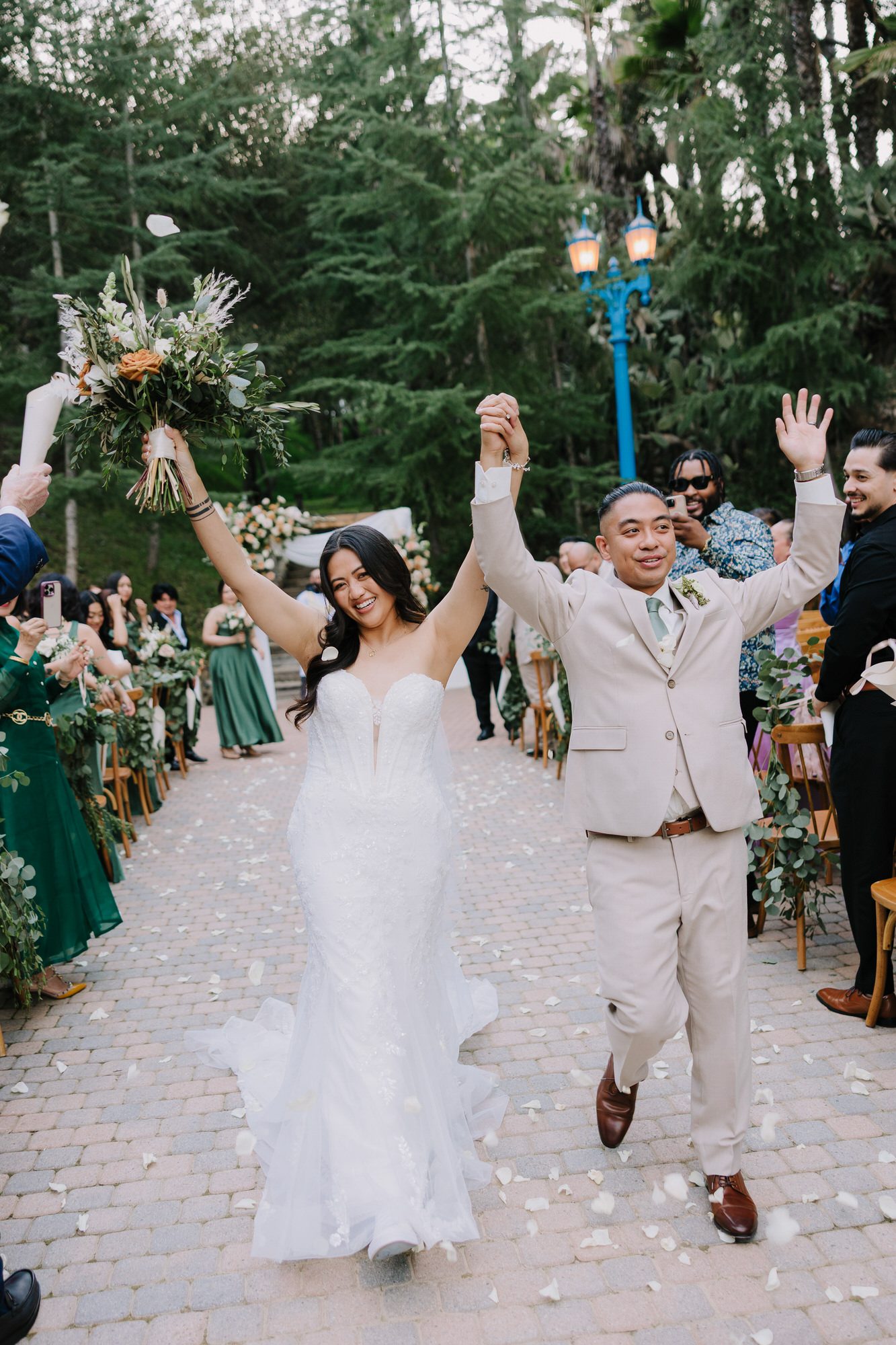 Bride and groom walking through a lush spring garden at Rancho Las Lomas with their three dogs and bridesmaids in pastel dresses.